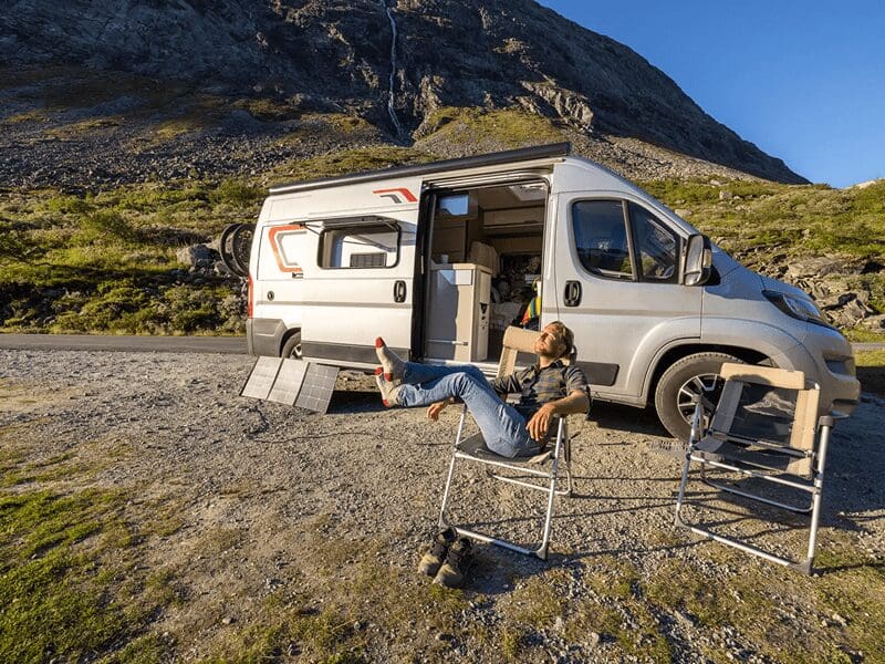 Man relaxing beside campervan in mountain landscape